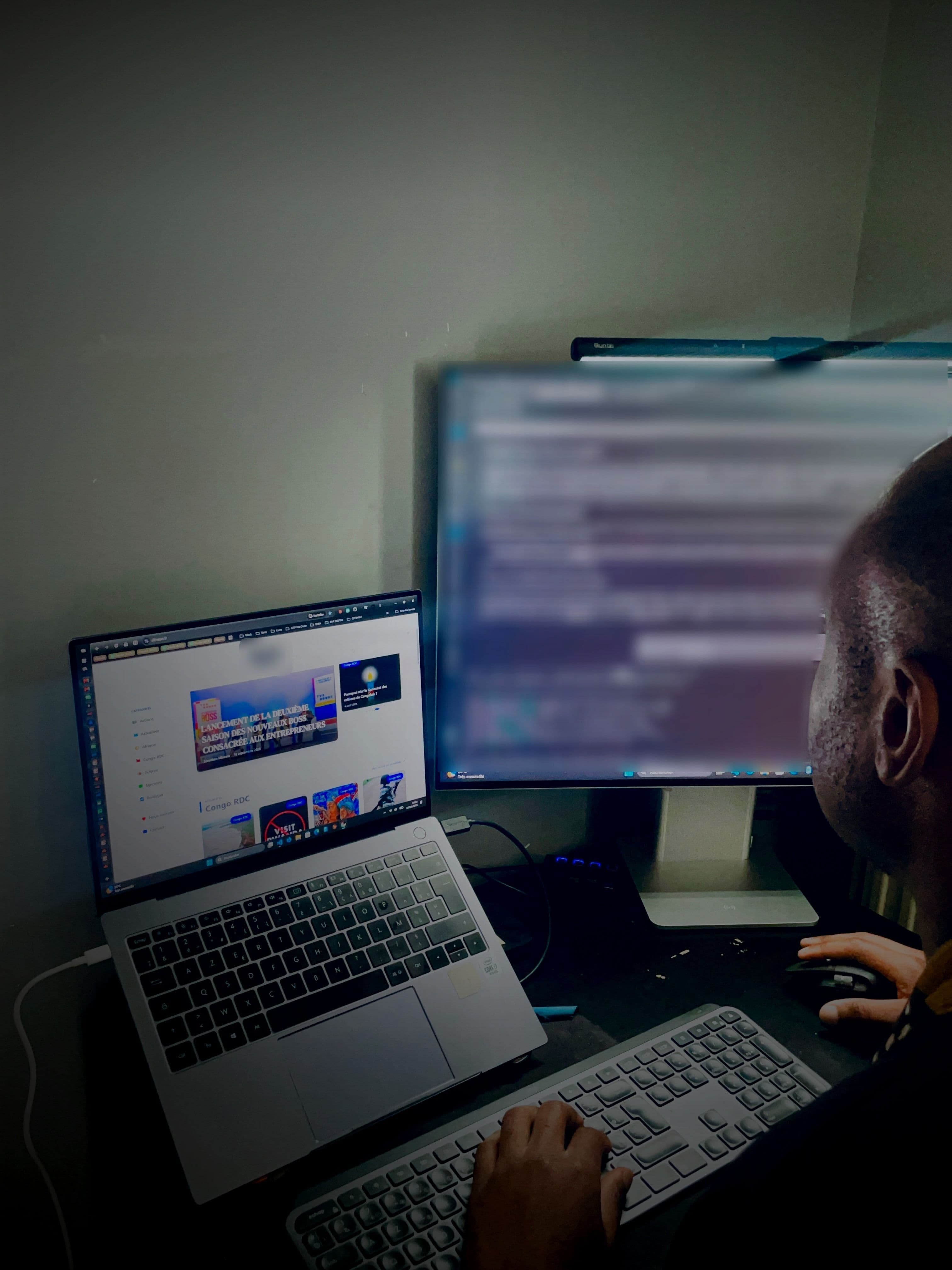 Poste de travail dans une pièce sombre : un site client affiché sur un portable, un second écran en arrière-plan.
